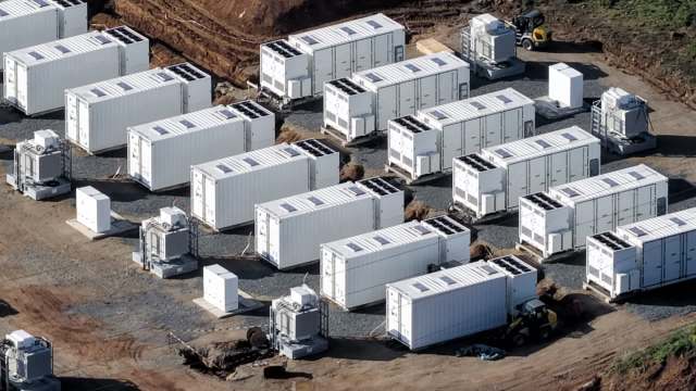 A densely packed array of white storage containers with solar panels, set on a gravel surface.