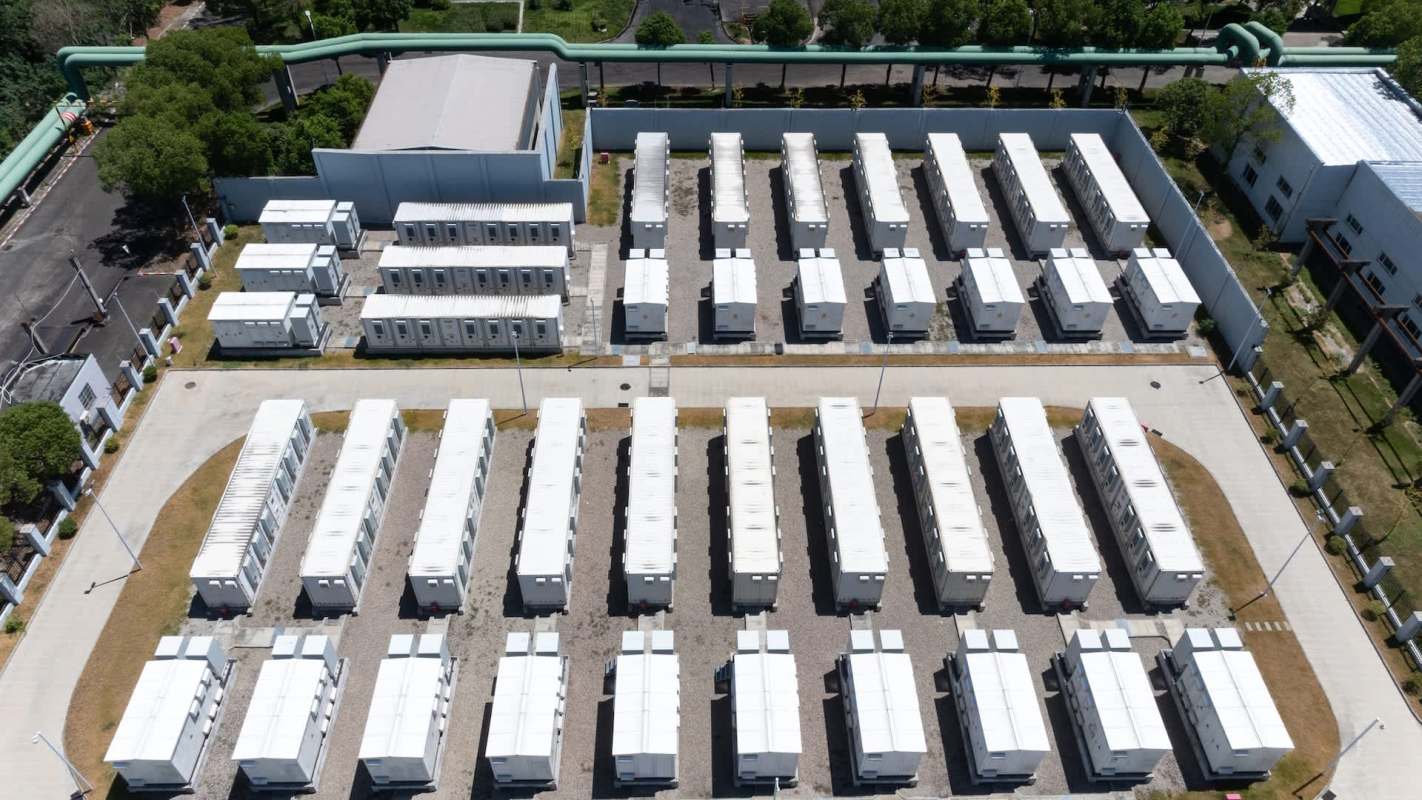 An aerial view of a neatly organized cluster of white shipping containers on a gravel lot.