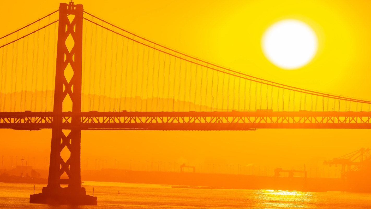 A silhouette of the Oakland Bay Bridge against a vibrant orange sunset.