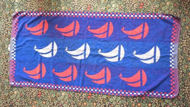 A blue blanket featuring a pattern of red and white sailboat designs on a floral background.