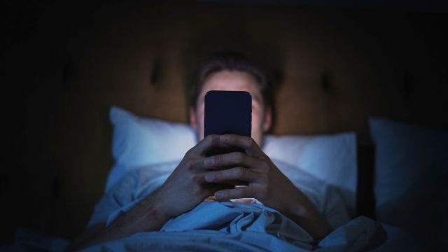 A person in bed uses a smartphone.