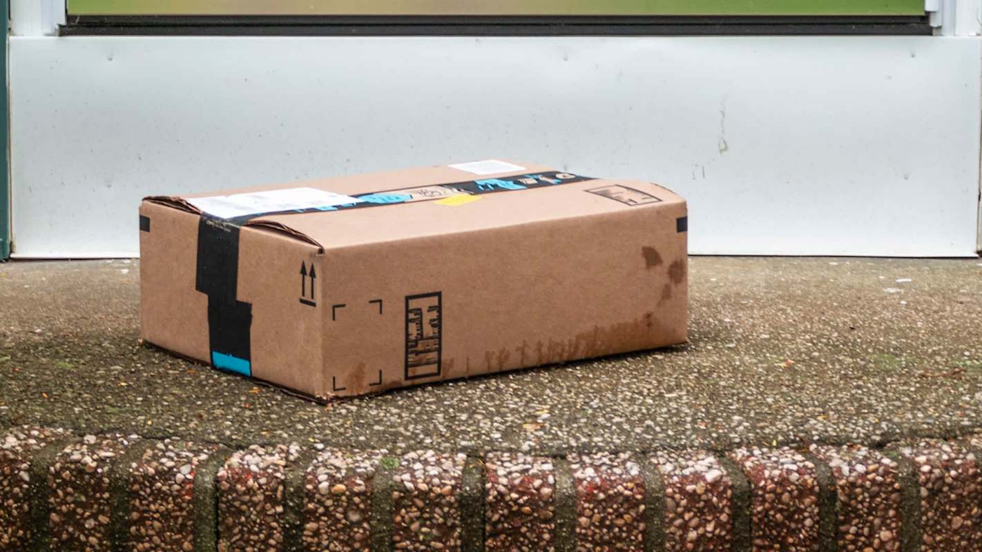 A cardboard package with tape sits on a doorstep, partially wet from rain.