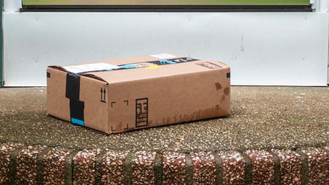 A cardboard package with tape sits on a doorstep, partially wet from rain.