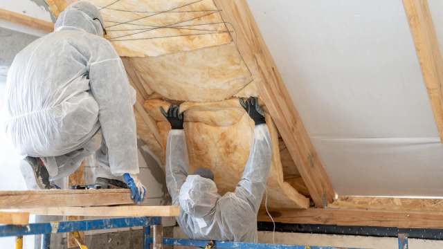 Two workers in protective suits install insulation in a ceiling.