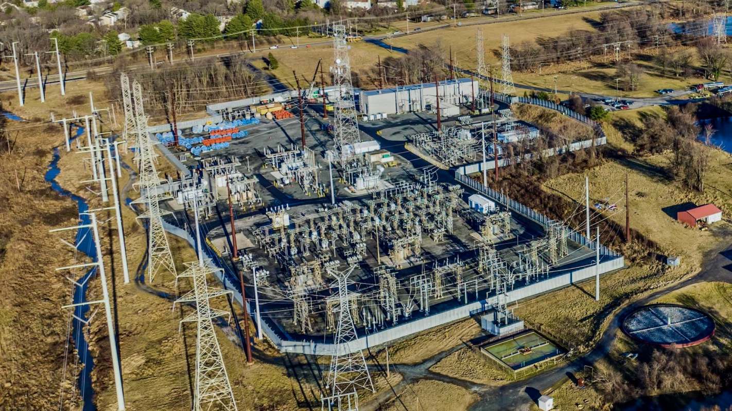 An aerial view of an electrical substation with transmission towers, surrounded by grassland and a small facility.