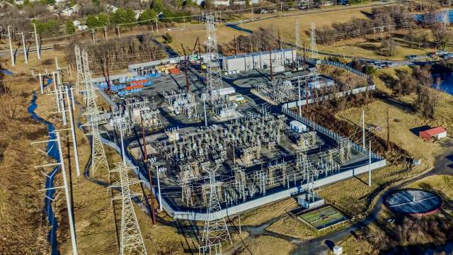 An aerial view of an electrical substation with transmission towers, surrounded by grassland and a small facility.