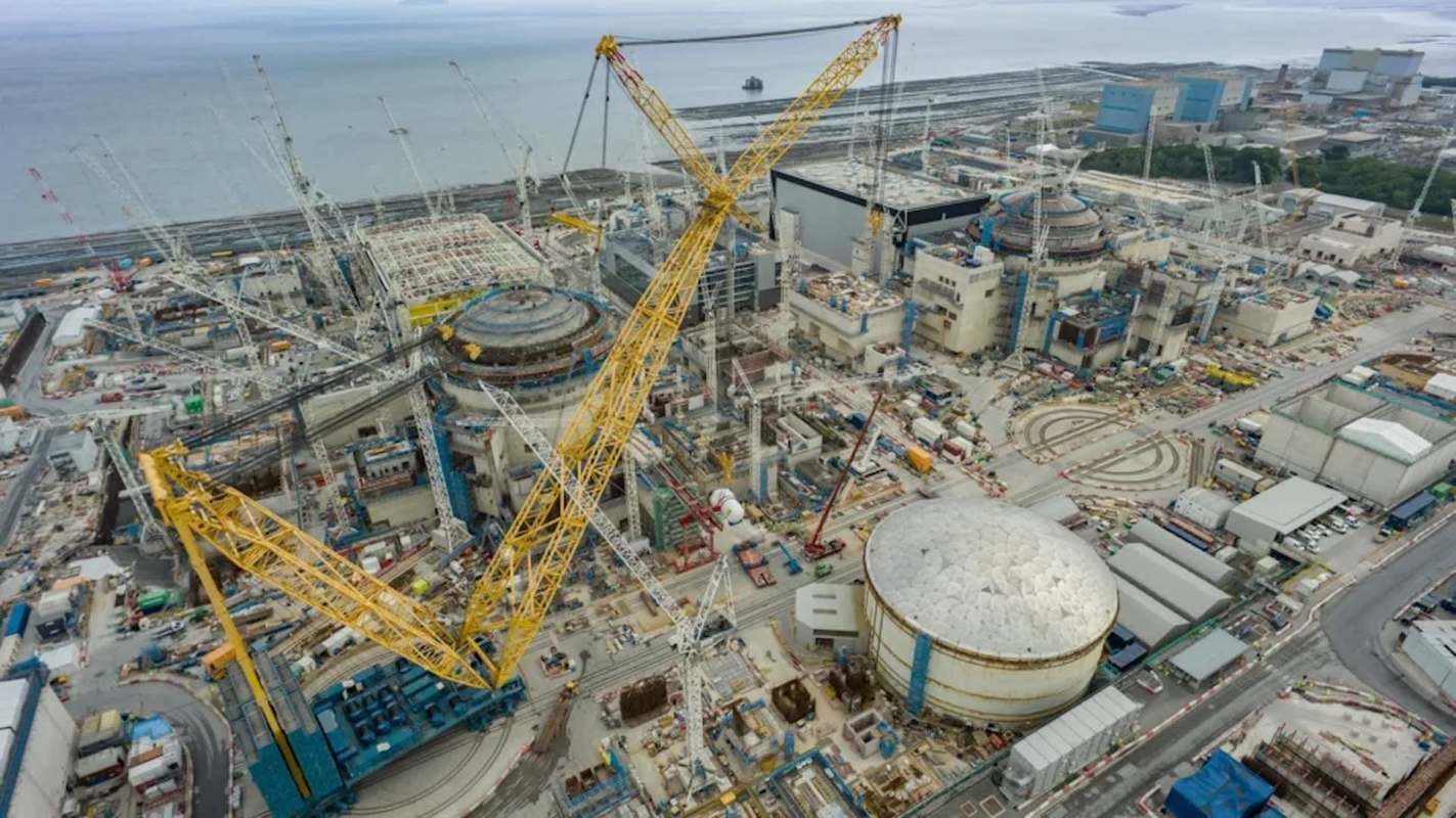 An aerial view of a large construction site featuring cranes and buildings near the coastline.