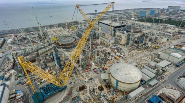 An aerial view of a large construction site featuring cranes and buildings near the coastline.