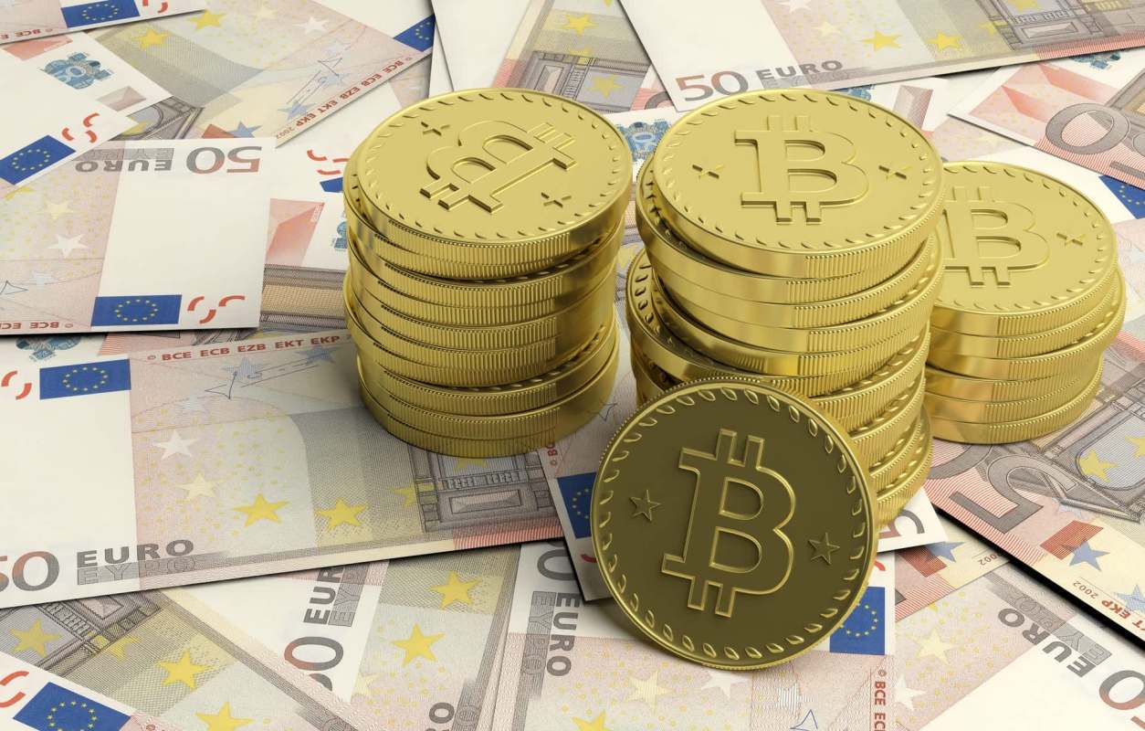 Stacks of gold Bitcoin coins on top of crumpled 50 Euro banknotes.