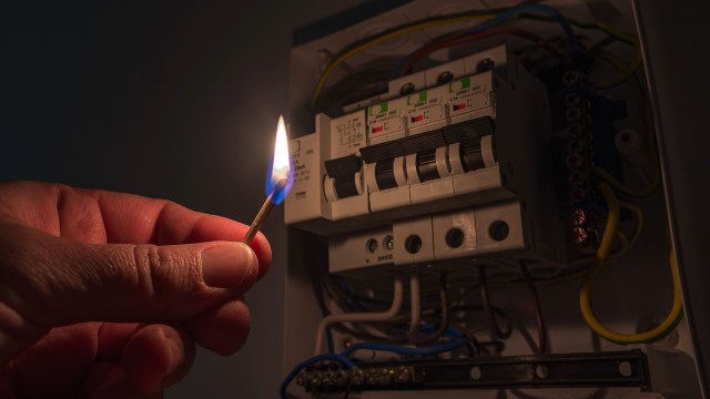 A hand illuminating an electrical panel with a match.