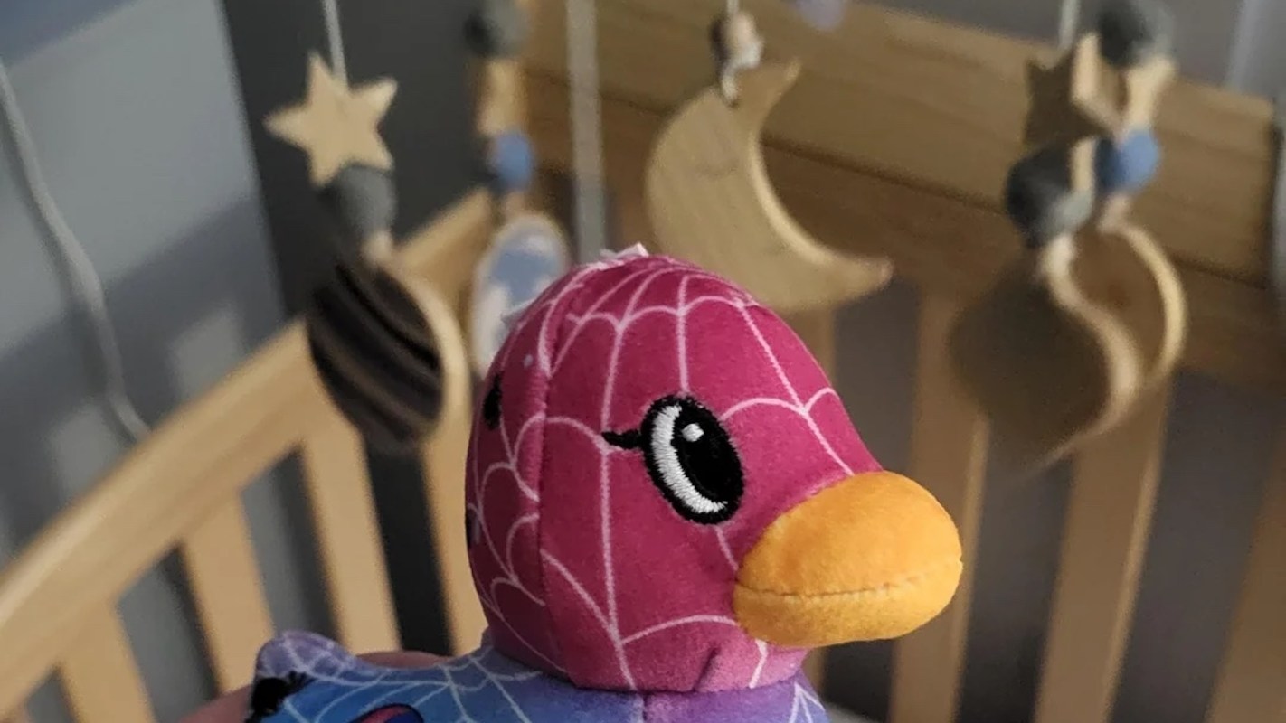 A plush duck with a spider web design in a nursery with hanging mobiles.