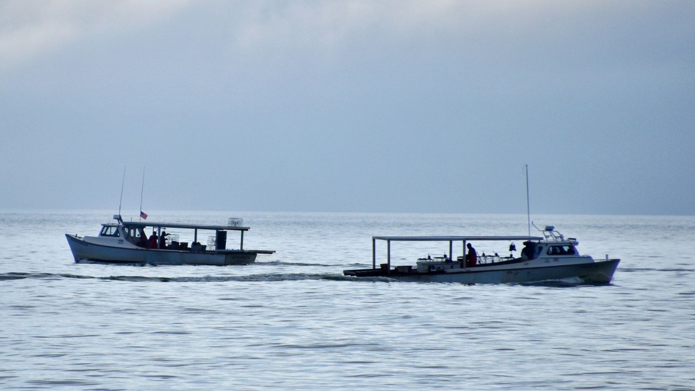 Two boats navigate through calm waters under a cloudy sky.