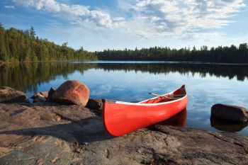 A red canoe rests on rocky shore in front of a lake.