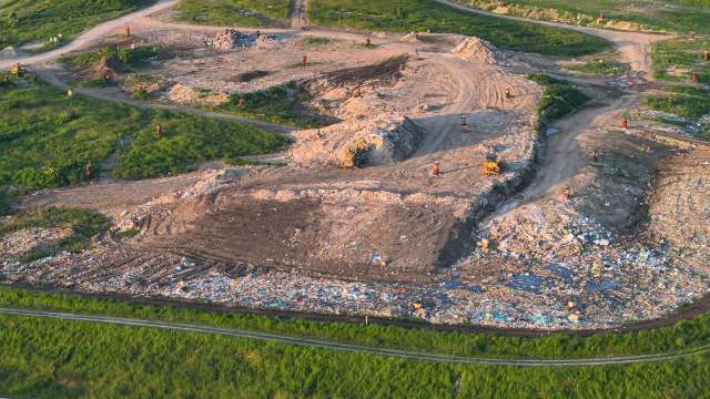 A wide view of a landfill with piles of trash on both sides and a dirt pathway in the center.