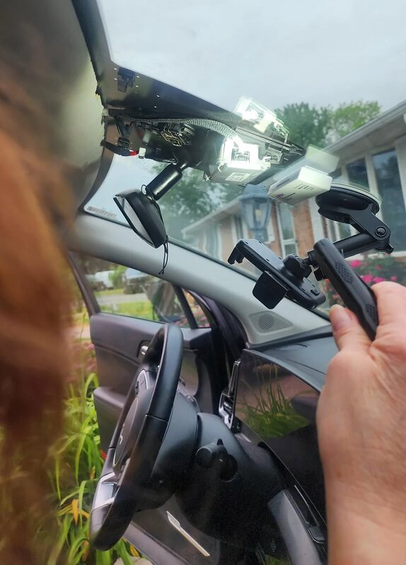 A person removing a dashboard camera on the windshield of a car.