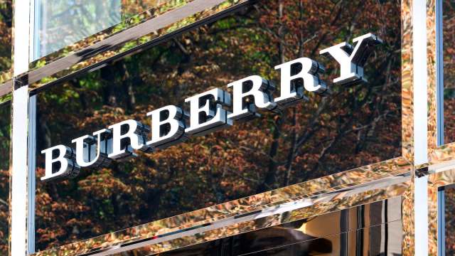 A close-up of a Burberry store sign reflecting autumn trees in the glossy surface.