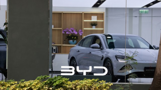 A sleek silver BYD car displayed in a modern showroom with decorative shelves in the background.