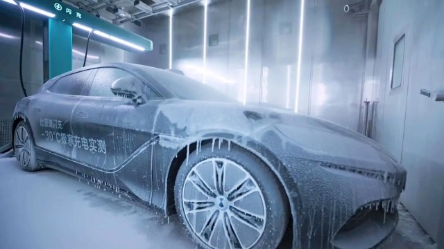 A BYD car is covered in foam and ice inside a charging station, showcasing extreme cold weather testing.