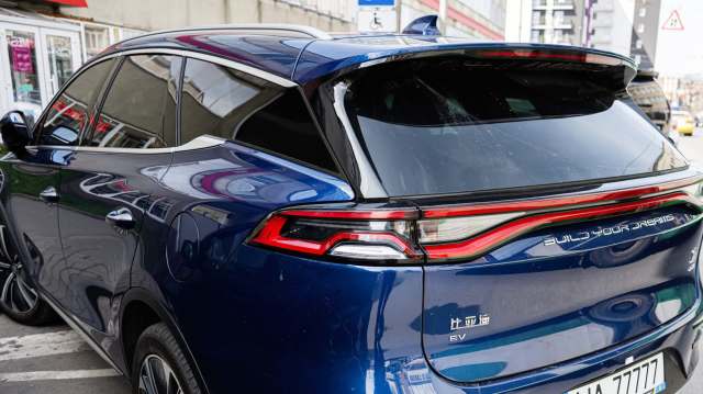 A blue electric BYD SUV parked on the street with a reflective window and modern tail lights.
