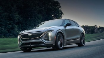 A sleek silver SUV driving on a winding road surrounded by greenery in the evening light.