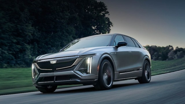 A sleek silver SUV driving on a winding road surrounded by greenery in the evening light.