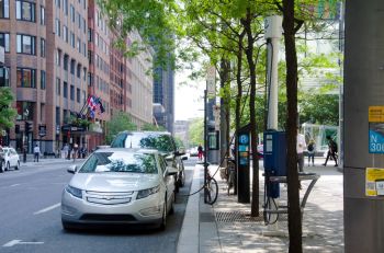 A silver car is parked and charging on a city street.