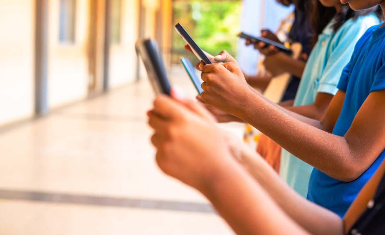 A group of young people holding and using smartphones in a well-lit corridor.