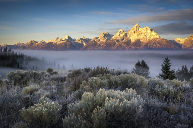 A panoramic view of snow-capped mountains rising above a foggy valley at dawn.