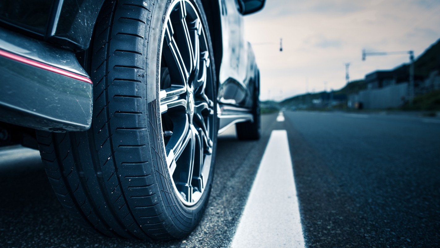 A close-up view of a car tire resting on an empty road with a blurred background.