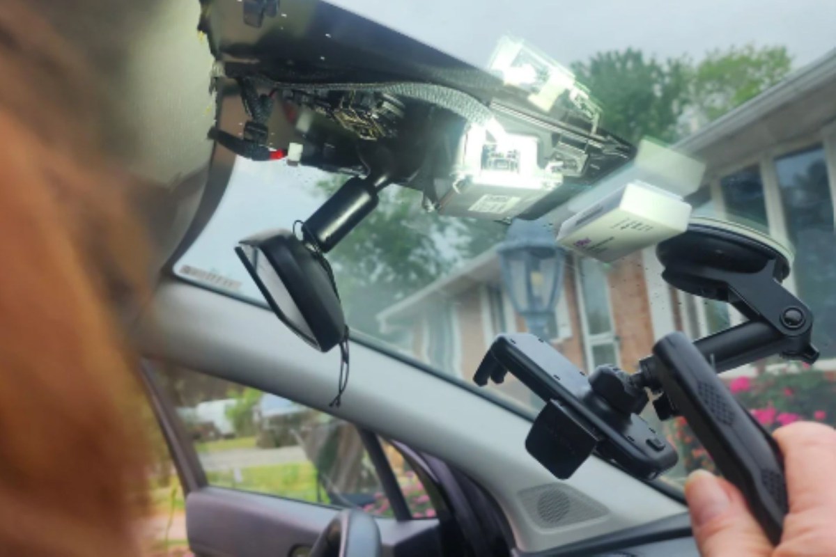 A person removing a dashboard camera on the windshield of a car.