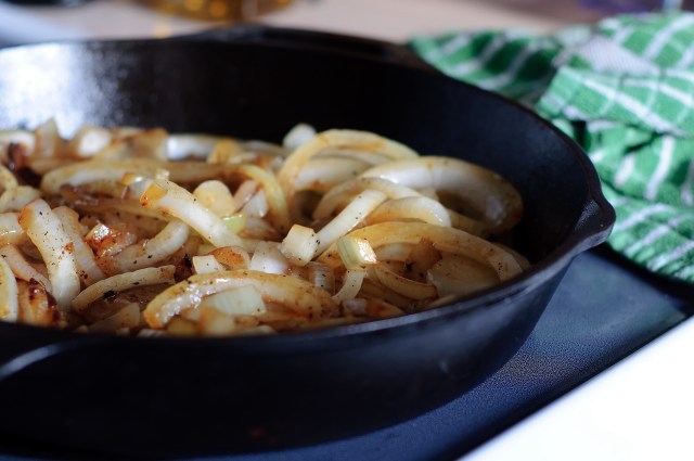 Sautéed onions in a black cast iron skillet with a green checkered towel in the background.