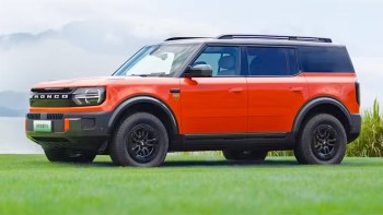 An orange Ford Bronco electric SUV parked on a grassy area with a scenic background.