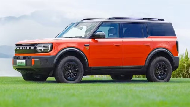 An orange Ford Bronco electric SUV parked on a grassy area with a scenic background.