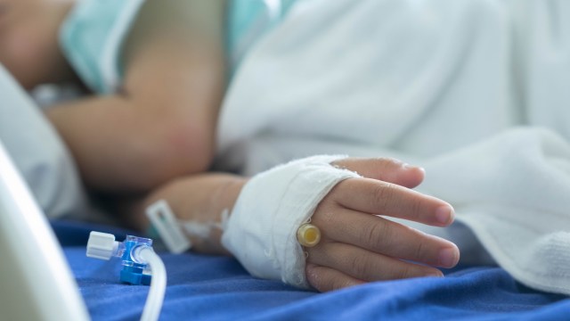 A close-up of a child's hand with a bandage and IV line in a hospital setting.