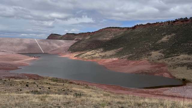 A reservoir surrounded by reddish hills under a cloudy sky, with a small boat near the shore.