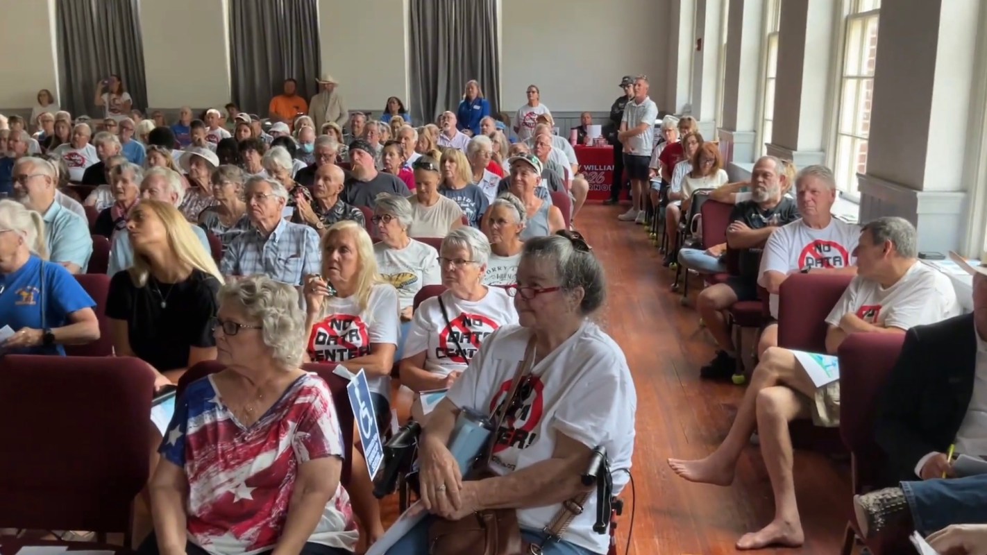 A large group of people, some wearing anti-data center shirts, attending a town hall.