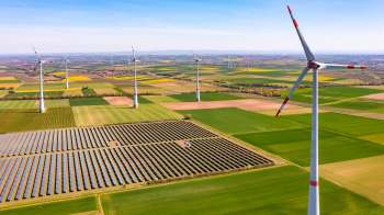 Aerial view of wind turbines near solar panels amidst vibrant agricultural fields.