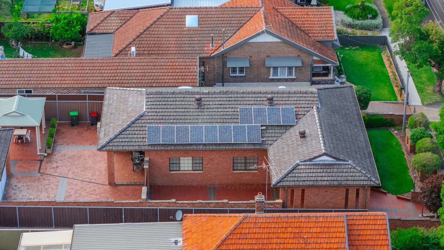 An aerial view of residential rooftops featuring solar panels, gardens, and patios.