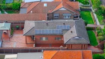 An aerial view of residential rooftops featuring solar panels, gardens, and patios.