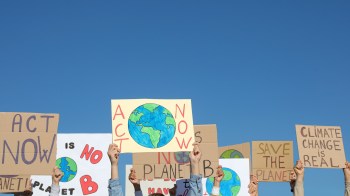 A group of protestors hold signs advocating for climate action against a clear blue sky.