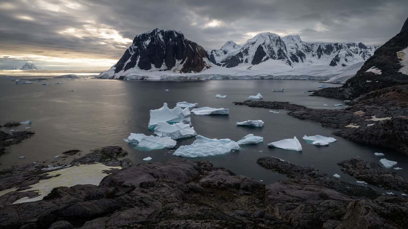 An Arctic landscape featuring floating icebergs and snow-capped mountains.