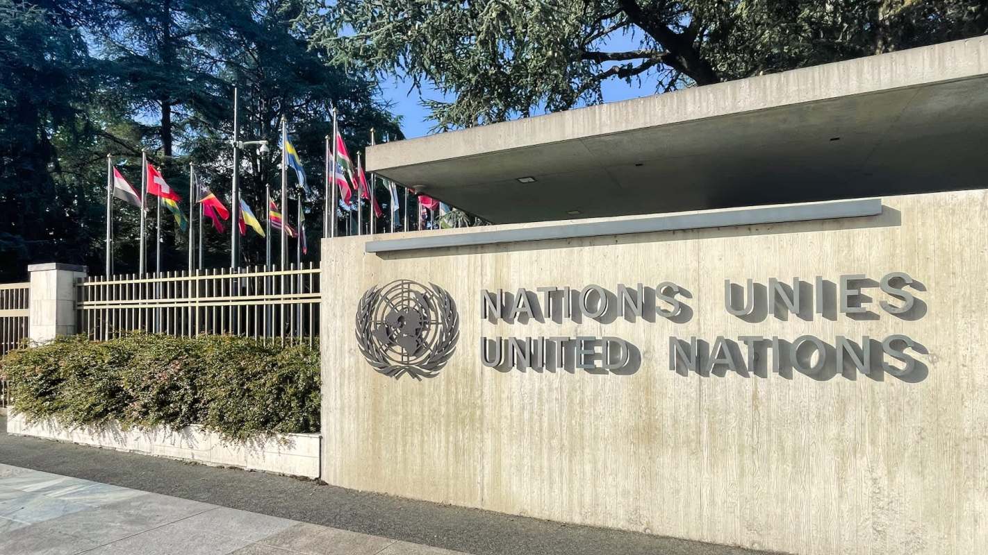 The United Nations entrance featuring the logo and various national flags lined up behind a concrete wall.