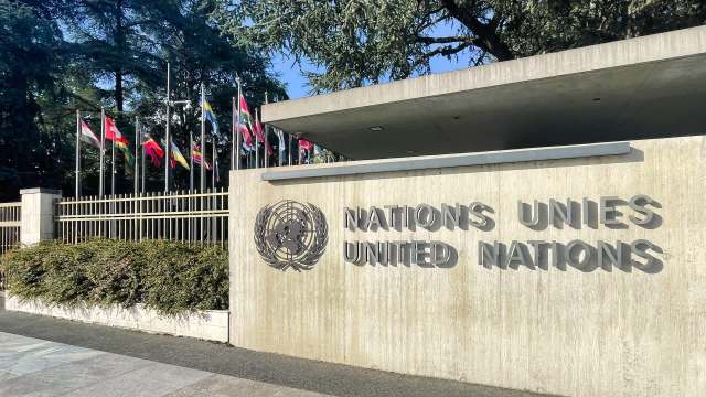 The United Nations entrance featuring the logo and various national flags lined up behind a concrete wall.
