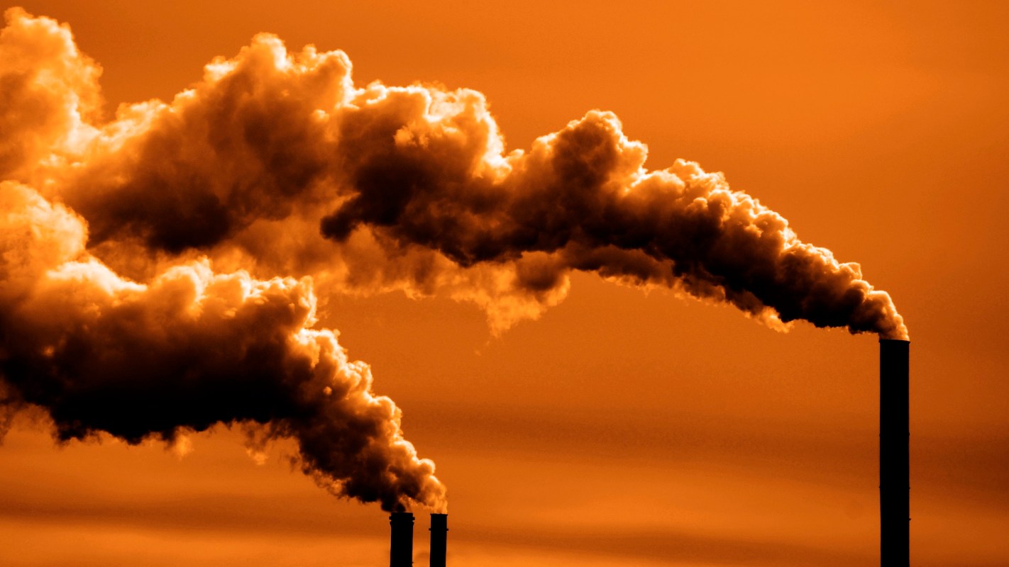 Smoke billows from industrial chimneys against a vibrant orange sky.