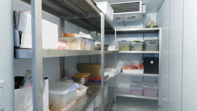 A clean and organized commercial refrigerator filled with labeled food containers on stainless steel shelves.