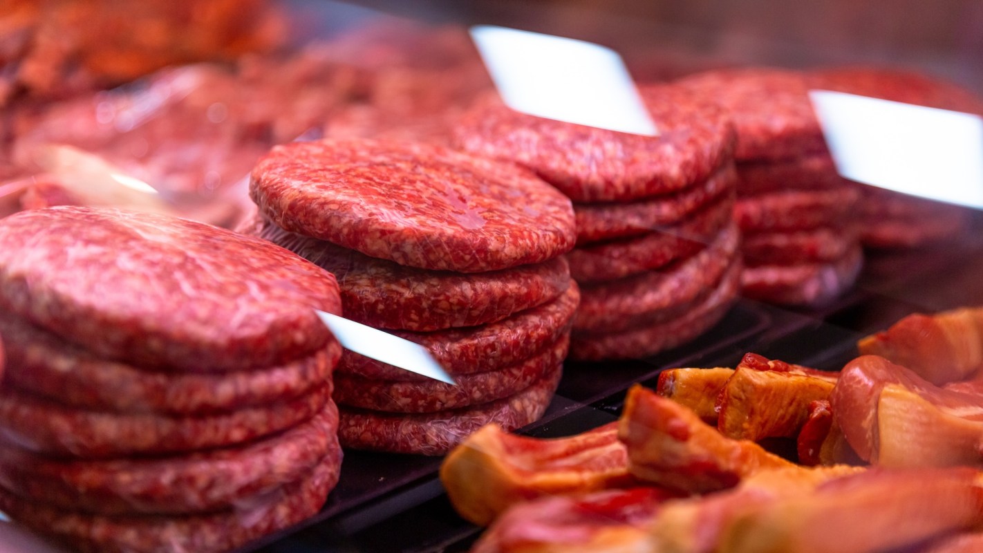 A display of fresh, round beef patties stacked with other meat products in a butcher shop.