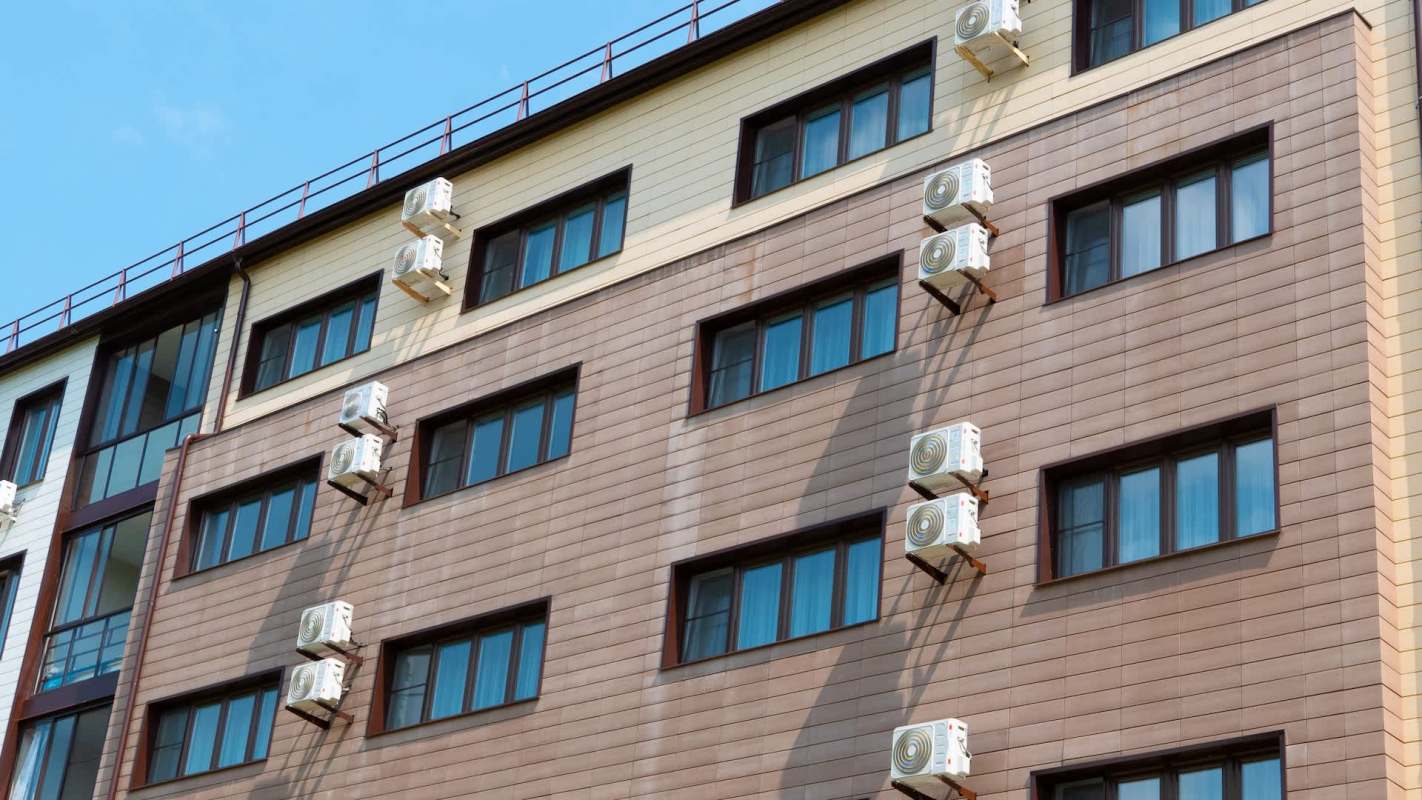 A multi-story building with multiple air conditioning units mounted on its exterior walls.