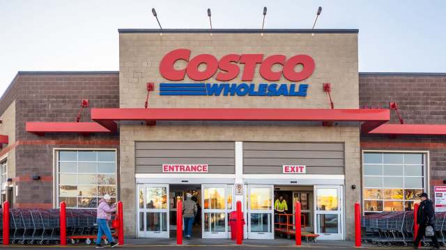 A Costco Wholesale store entrance with shoppers and shopping carts outside on a clear day.