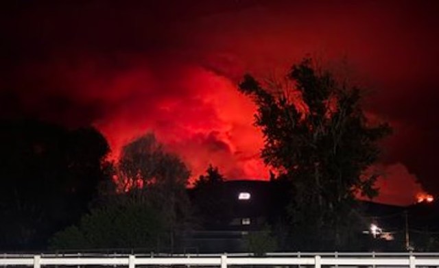 A night sky illuminated by a large fire, casting an eerie red glow.