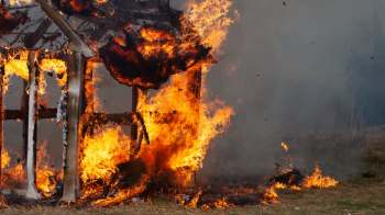 A wooden structure engulfed in flames with bright orange fire and smoke billowing around.